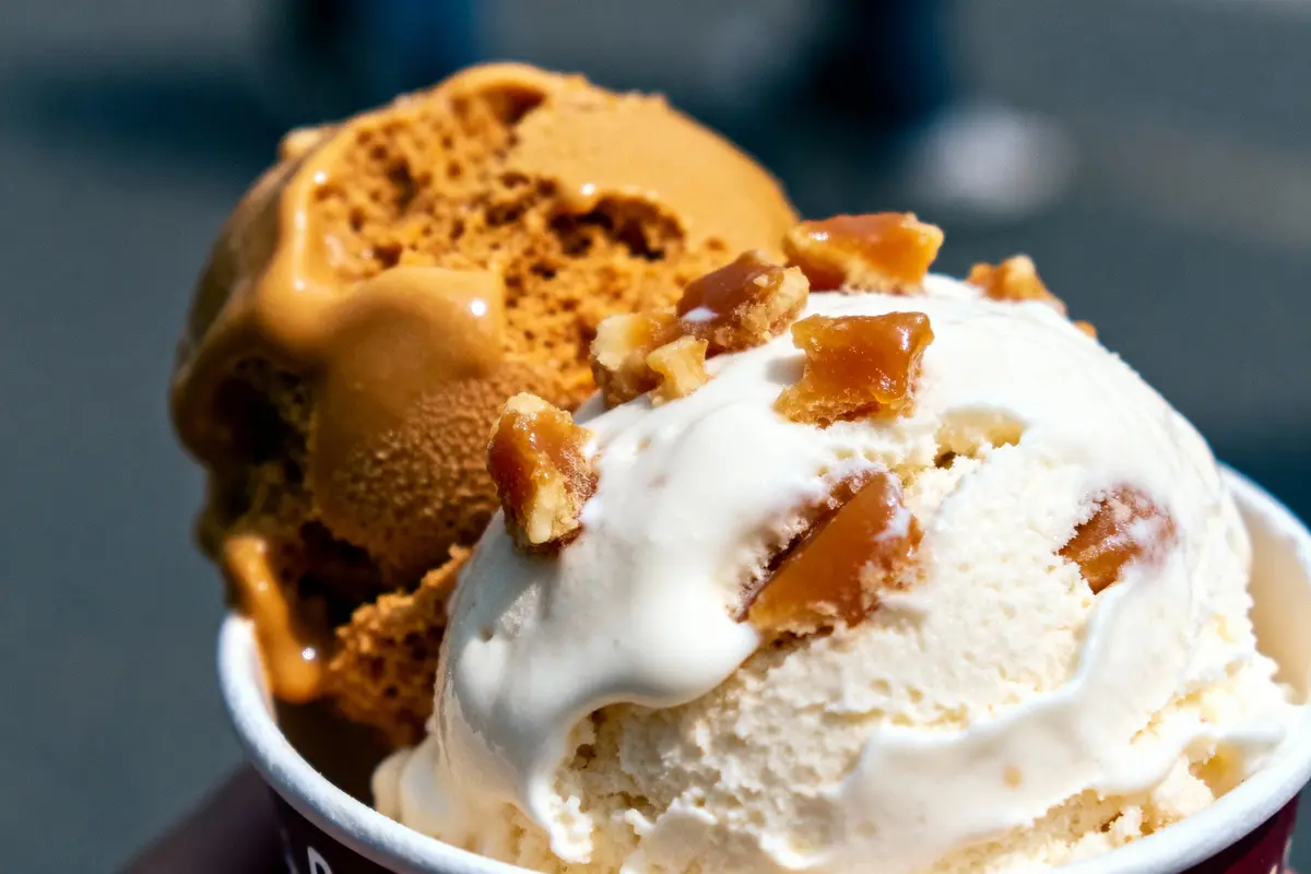 Deux boules de glace, une caramel et une vanille, avec morceaux croquants, dans un pot.