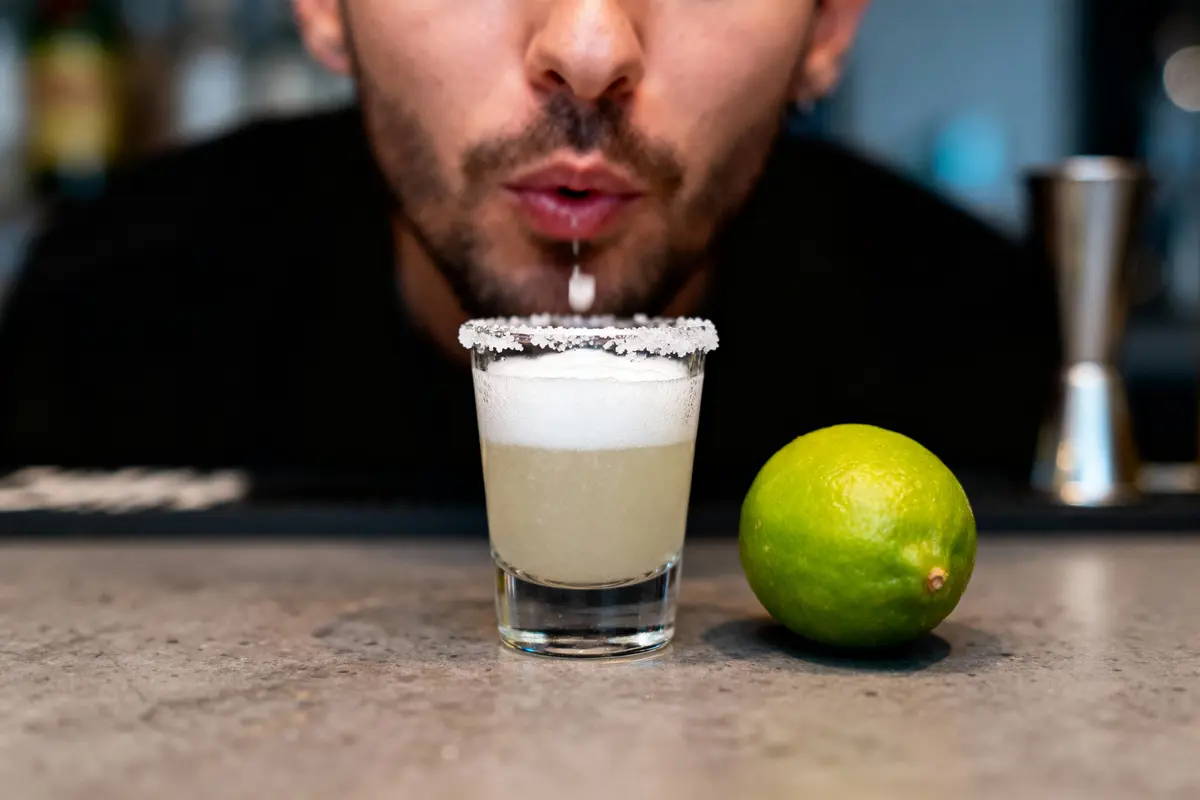 pexels-michal-pech-213601-757318 (1) Homme soufflant mousse sur verre Margarita, lime à côté, bar en arrière-plan flou.
