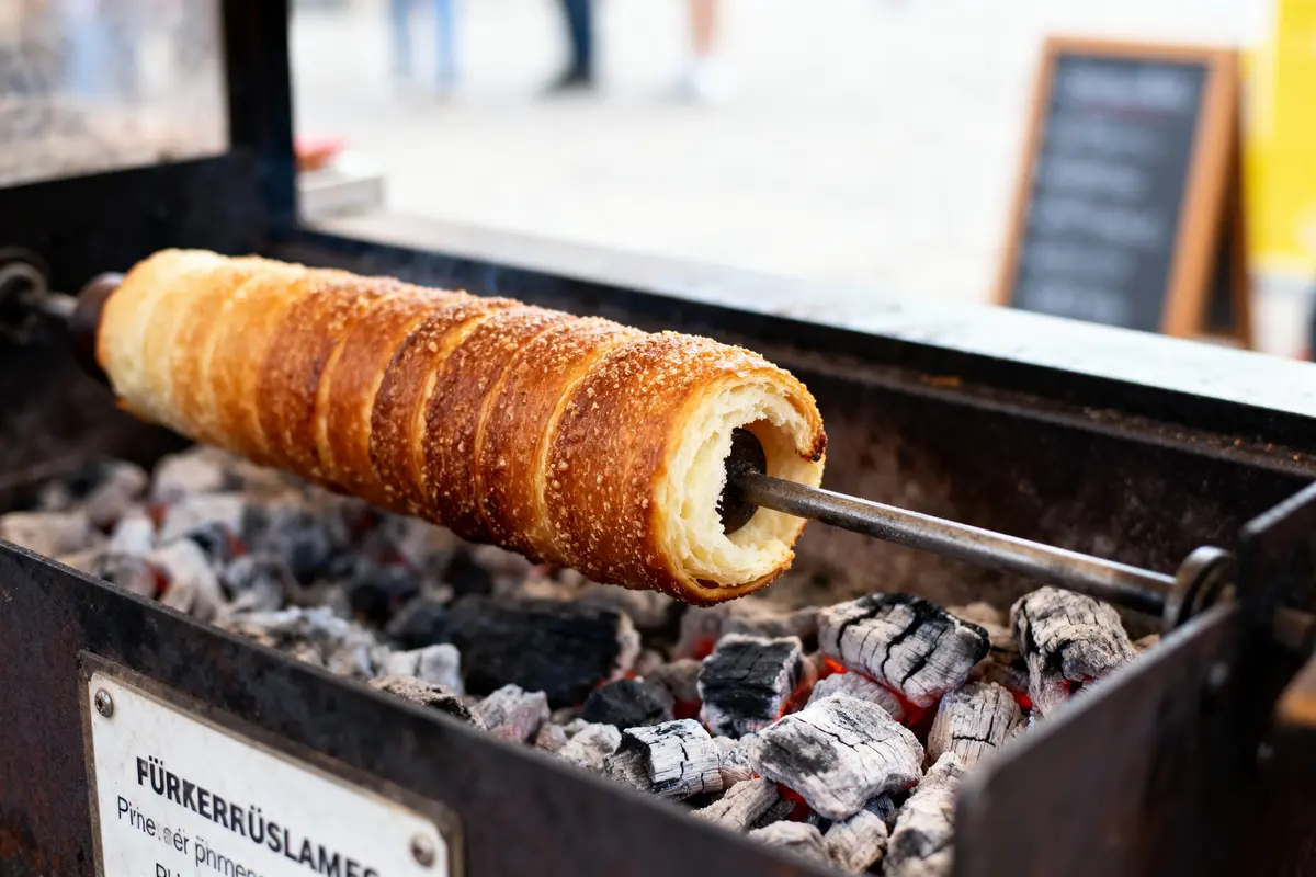 Trdelník grillé sur charbon de bois, avec une croûte dorée et sucrée, en cuisson sur rôtissoire.