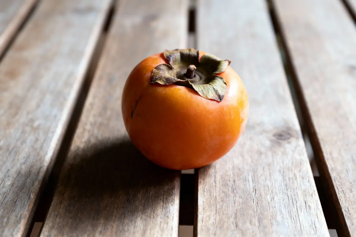 Un kaki orange sur une table en bois, éclairage naturel doux.