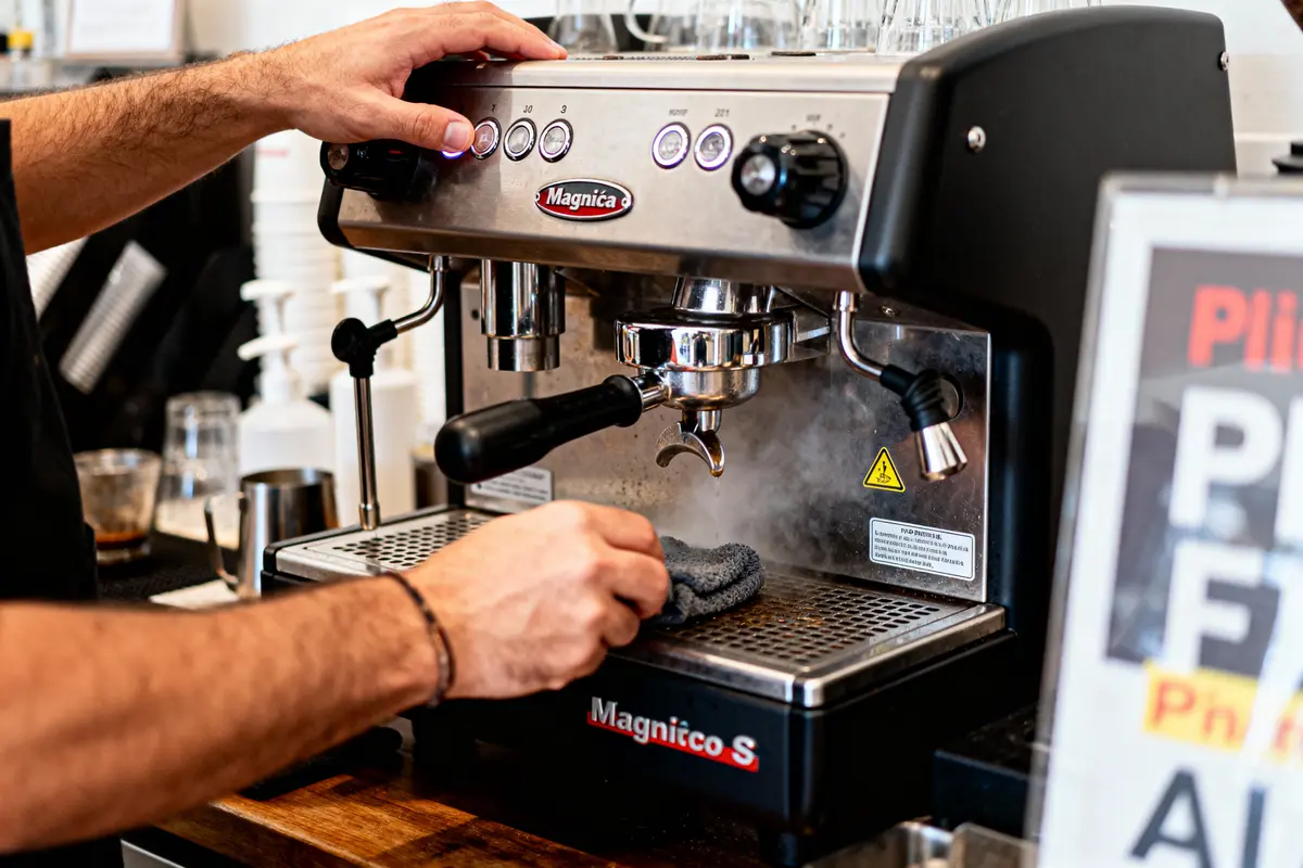 Barista nettoyant machine à café Magnifica S avec un chiffon, boutons et becs visibles, intérieur café.