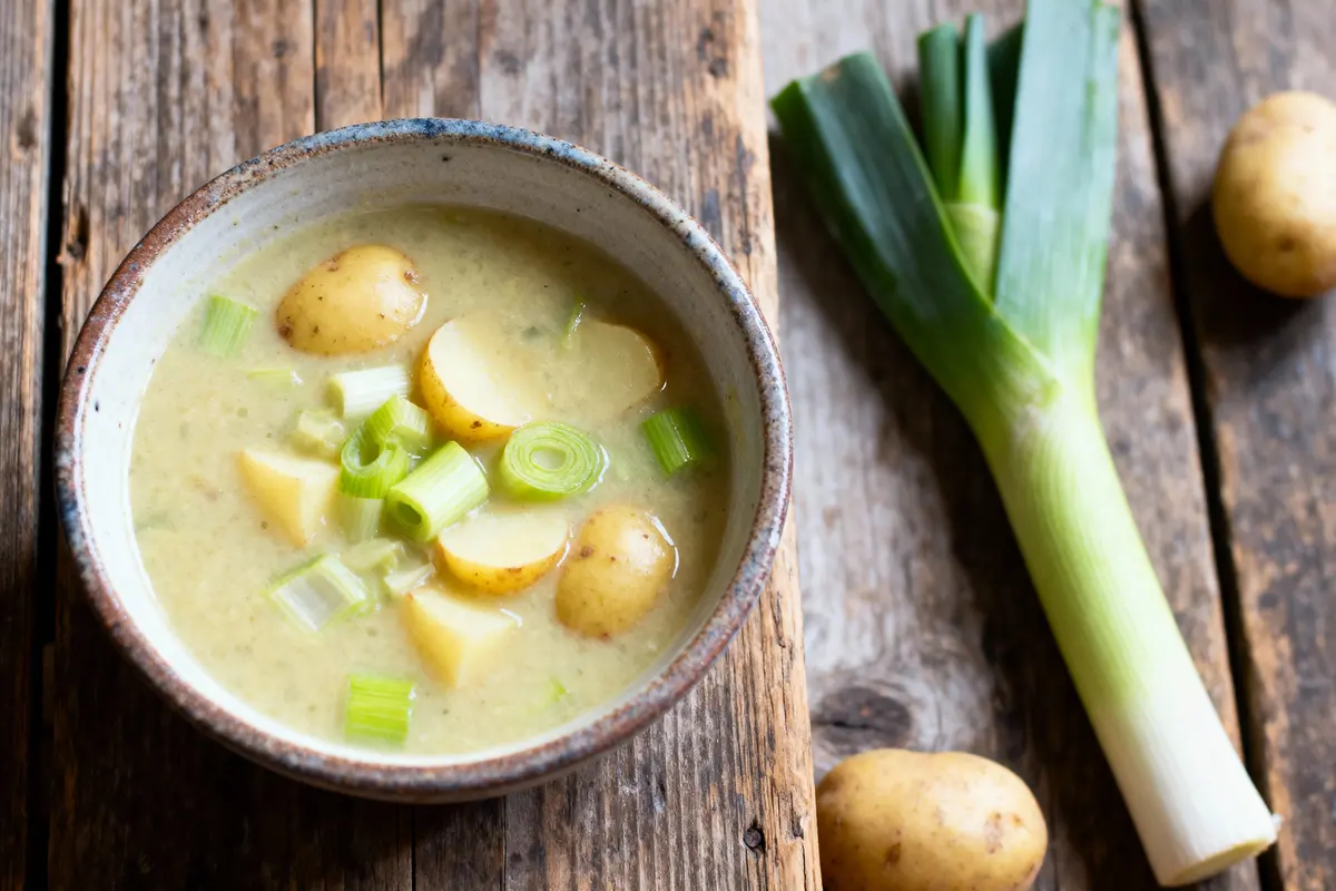 pexels-michal-pech-213601-757318 (1) Bol de soupe aux poireaux et pommes de terre, à côté d'un poireau frais et pommes de terre entières.