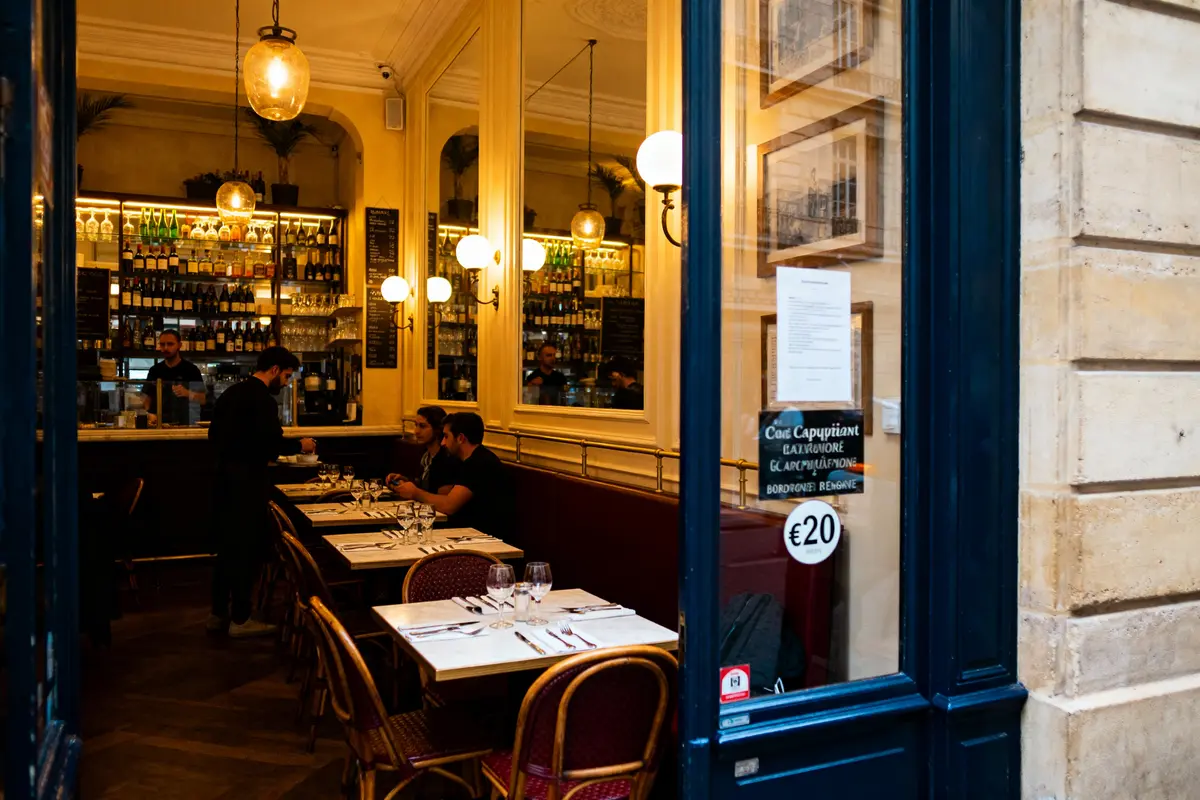 pexels-michal-pech-213601-757318 (1) Intérieur chaleureux d'un café parisien avec des tables dressées et des clients assis, éclairage tamisé.