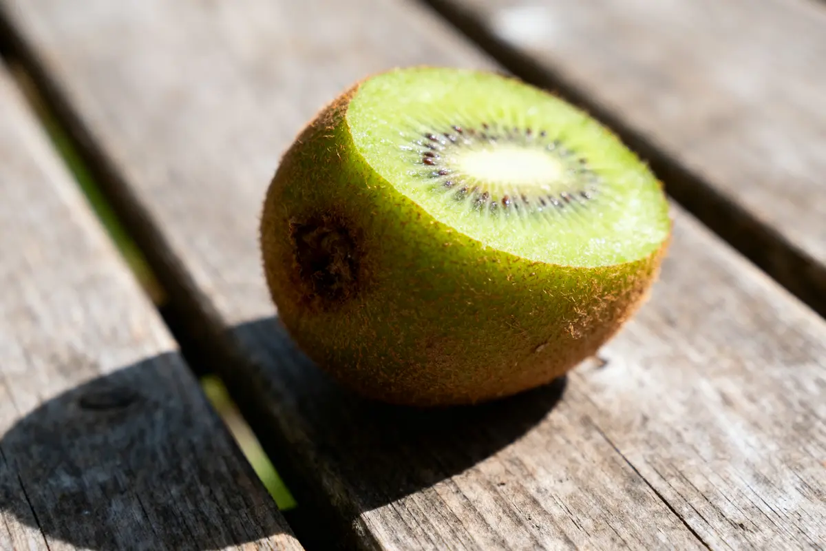 pexels-michal-pech-213601-757318 (1) Moitié de kiwi mûr posé sur une table en bois, éclairée par le soleil.