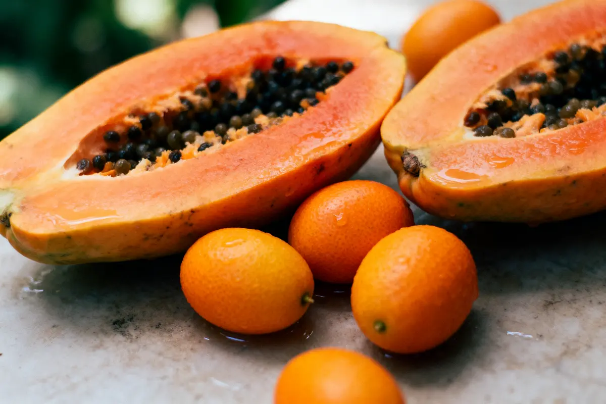 pexels-michal-pech-213601-757318 (1) Papaye mûre coupée en deux avec plusieurs kumquats sur une surface en marbre.