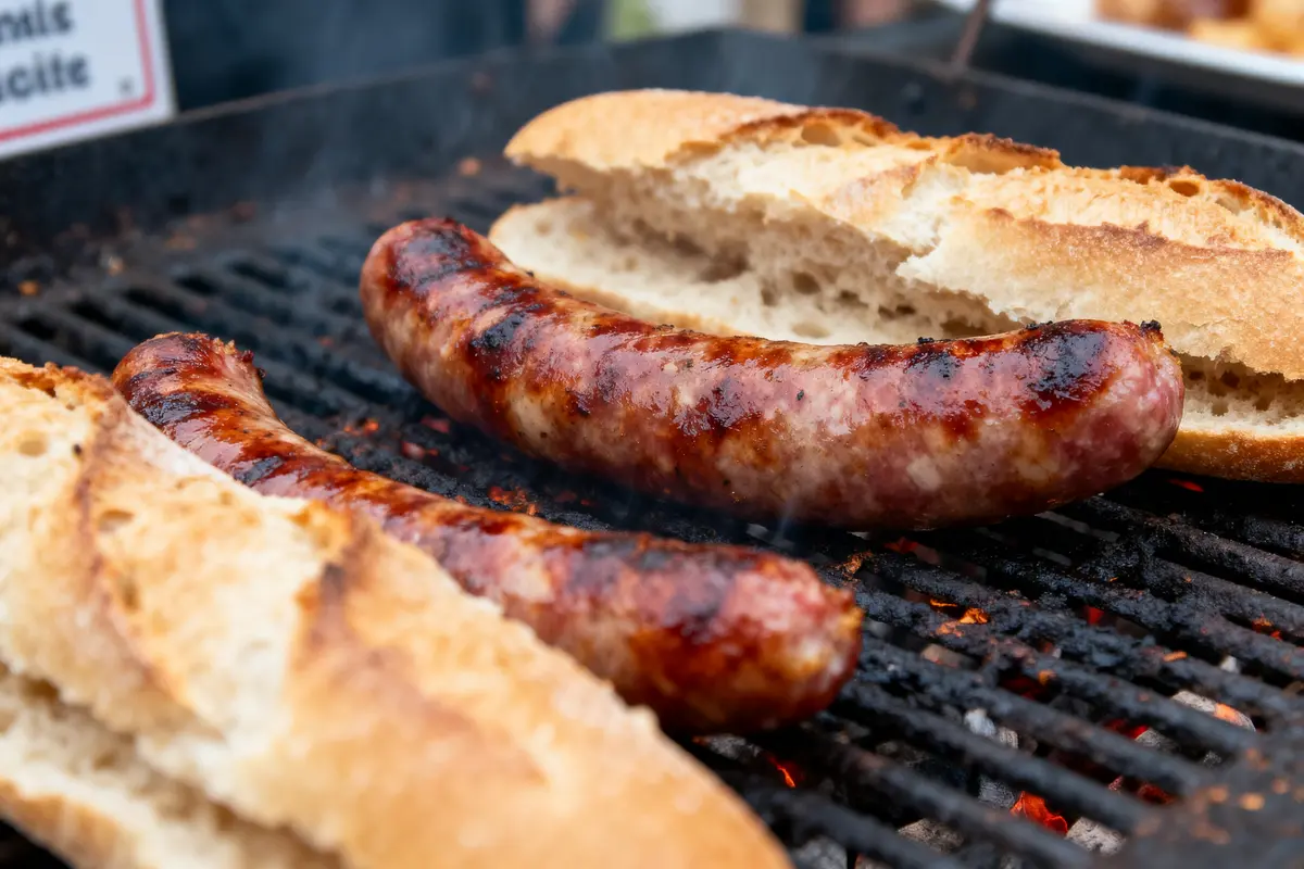 Saucisses grillées avec du pain sur un barbecue fumant. Options de repas en plein air.