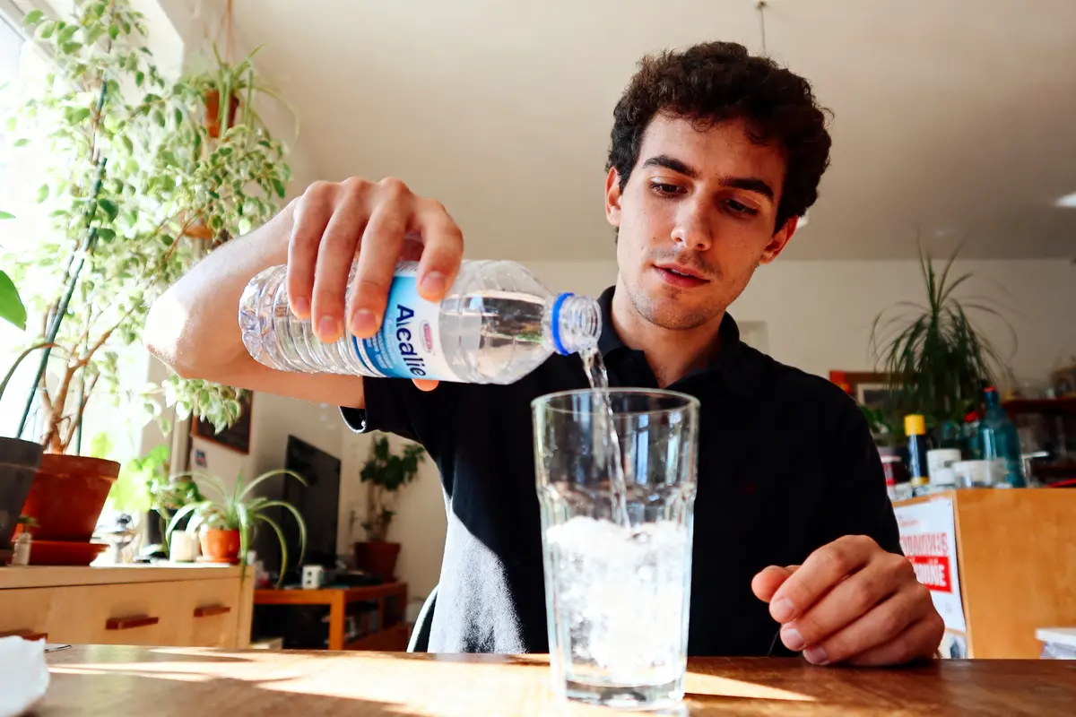pexels-michal-pech-213601-757318 (1) Homme versant de l'eau en bouteille dans un verre, intérieur lumineux, plantes en arrière-plan.