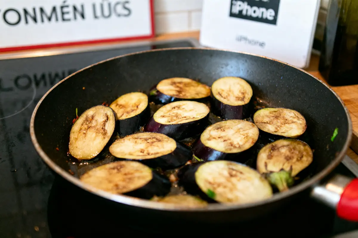 pexels-michal-pech-213601-757318 (1) Tranches d'aubergine grillées dans une poêle noire, avec arrière-plan flou et enseignes visibles.