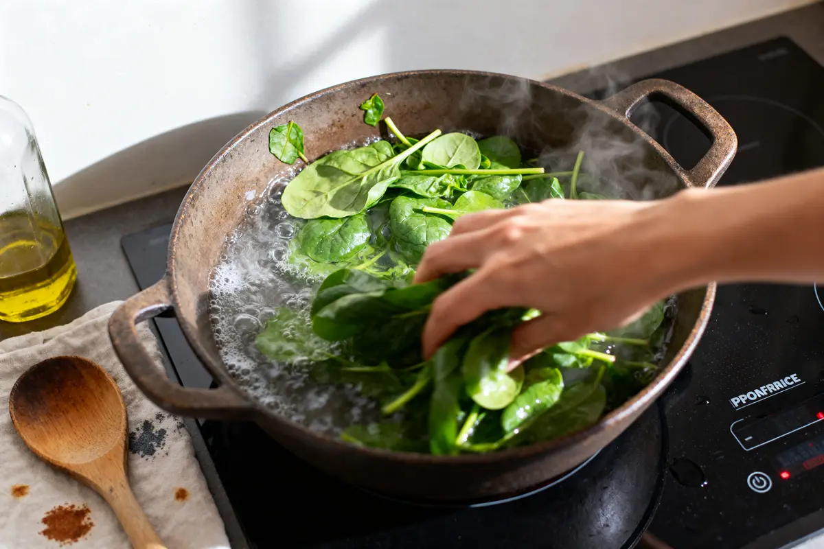 Main ajoutant des épinards frais à l'eau bouillante pour cuisson des épinards frais